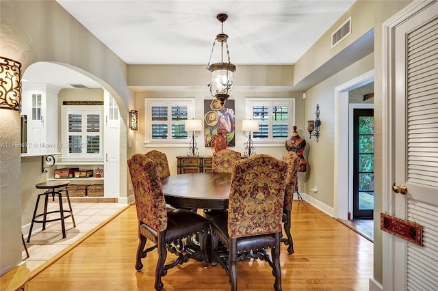 dining area with light wood-style floors, arched walkways, visible vents, and baseboards