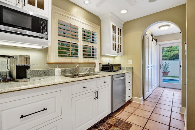 kitchen with arched walkways, light tile patterned floors, stainless steel appliances, glass insert cabinets, and a sink