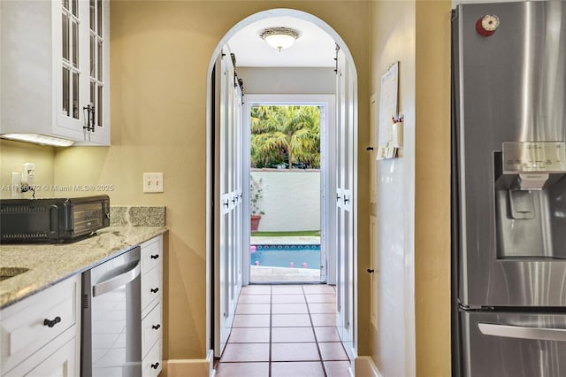 kitchen featuring arched walkways, light stone counters, stainless steel appliances, white cabinetry, and glass insert cabinets