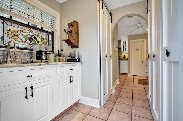 bar featuring arched walkways, light tile patterned flooring, a sink, a ceiling fan, and baseboards