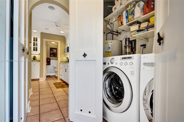 laundry room featuring arched walkways, light tile patterned flooring, washing machine and dryer, electric water heater, and laundry area