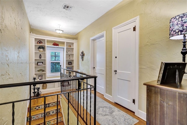 corridor with visible vents, a textured wall, a textured ceiling, an upstairs landing, and wood finished floors