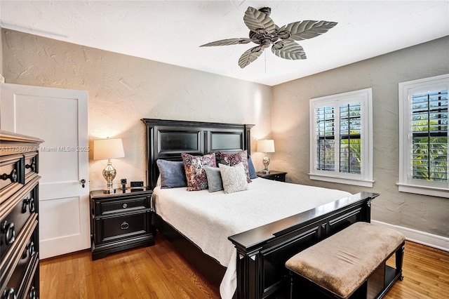 bedroom featuring baseboards, a ceiling fan, wood finished floors, and a textured wall