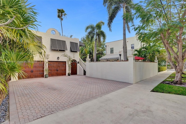 view of front of house featuring solar panels, decorative driveway, fence, and stucco siding