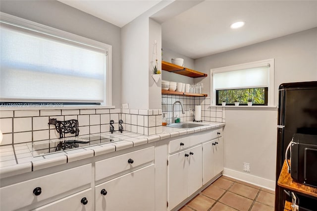 kitchen featuring tile countertops, open shelves, tasteful backsplash, a sink, and black appliances