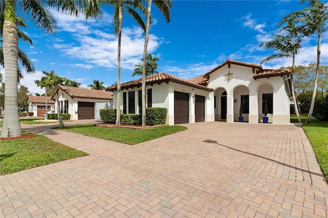 mediterranean / spanish-style home with a garage, a tile roof, decorative driveway, stucco siding, and a front lawn