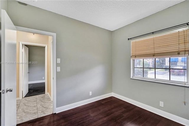 unfurnished room with a textured ceiling, baseboards, and wood finished floors