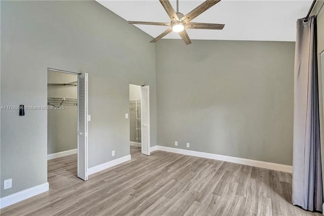 unfurnished bedroom featuring baseboards, ceiling fan, a spacious closet, light wood-style floors, and high vaulted ceiling