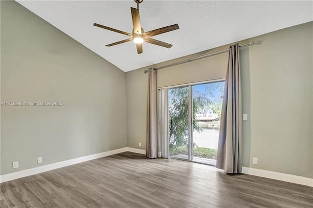 empty room with baseboards, a ceiling fan, wood finished floors, a water view, and vaulted ceiling