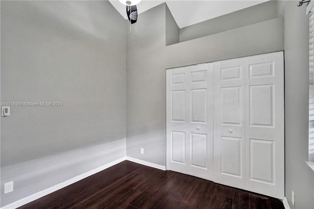 unfurnished bedroom with dark wood-type flooring, a closet, and baseboards