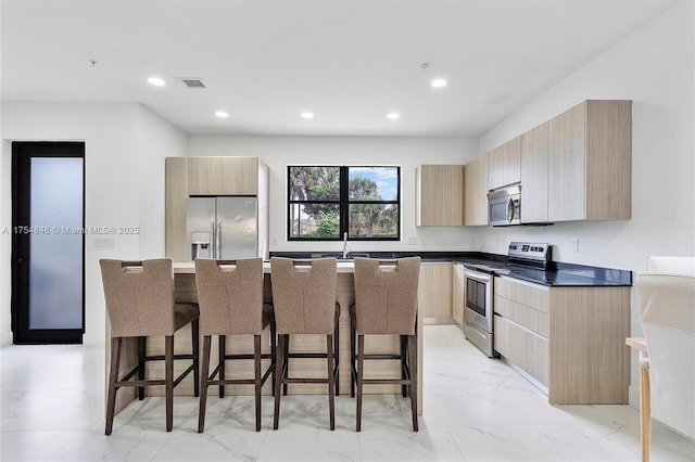 kitchen with visible vents, appliances with stainless steel finishes, light brown cabinets, modern cabinets, and a kitchen bar