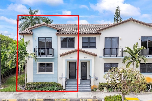 view of front of home featuring a balcony, a tile roof, and stucco siding