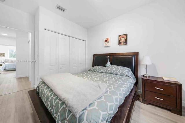 bedroom with light wood-style flooring, visible vents, and a closet