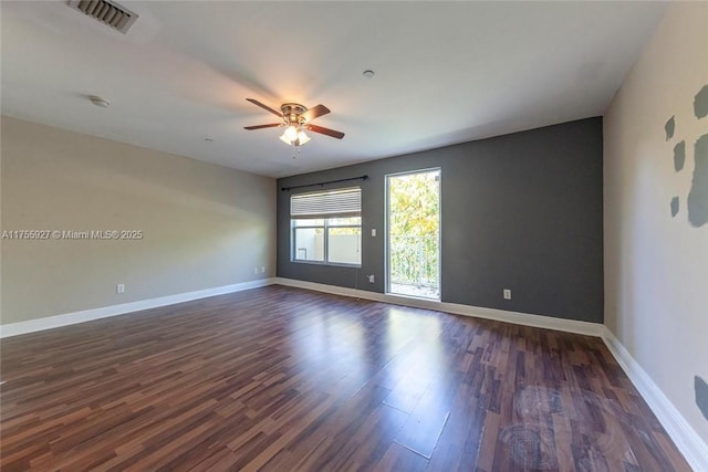 spare room featuring dark wood-style floors, ceiling fan, visible vents, and baseboards