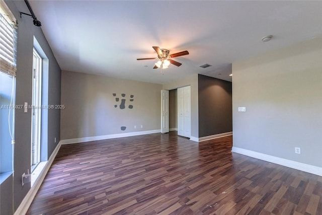 unfurnished room featuring a ceiling fan, baseboards, visible vents, and dark wood-style flooring