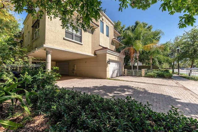 view of side of home featuring a garage, decorative driveway, fence, and stucco siding