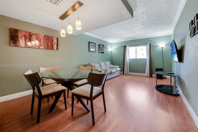 dining room featuring a textured ceiling, crown molding, wood finished floors, and baseboards