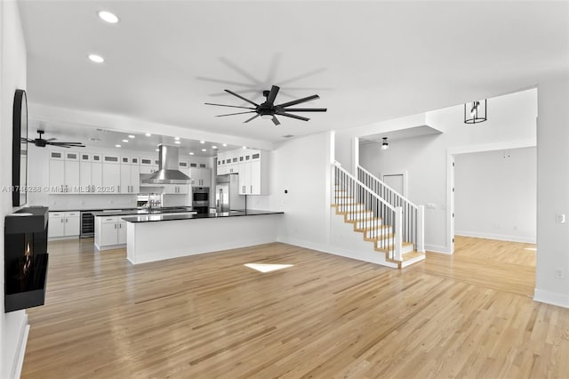 unfurnished living room with a ceiling fan, wine cooler, light wood-style flooring, and stairway