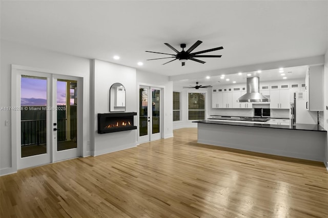 unfurnished living room with ceiling fan, a lit fireplace, french doors, light wood-type flooring, and recessed lighting