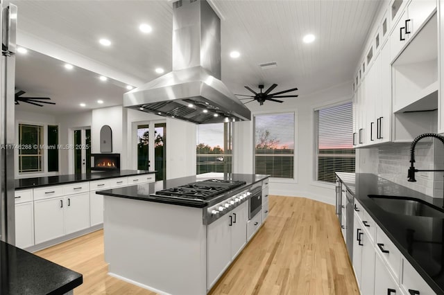 kitchen featuring island exhaust hood, dark countertops, a ceiling fan, a kitchen island, and gas cooktop