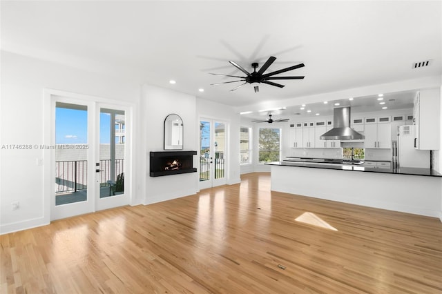 unfurnished living room featuring a warm lit fireplace, recessed lighting, visible vents, baseboards, and light wood finished floors