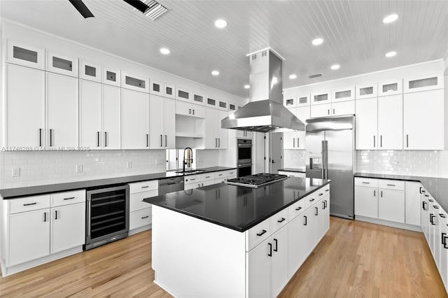 kitchen featuring island range hood, dark countertops, wine cooler, appliances with stainless steel finishes, and a sink