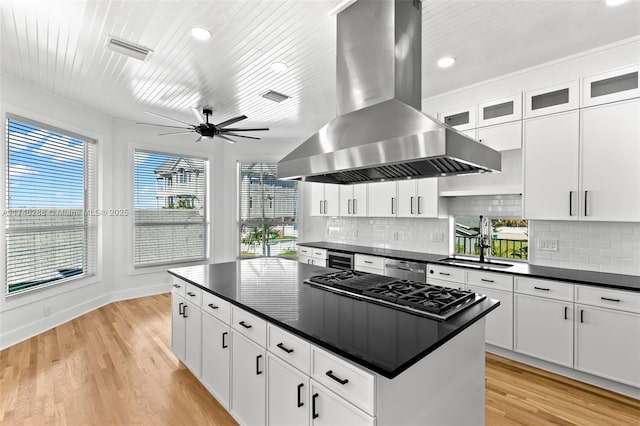 kitchen with dark countertops, visible vents, a sink, gas cooktop, and island range hood