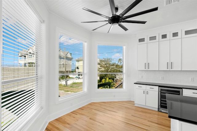 interior space with beverage cooler, ornamental molding, light wood-style flooring, and a wealth of natural light