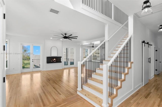 stairway featuring a warm lit fireplace, visible vents, ceiling fan, wood finished floors, and french doors