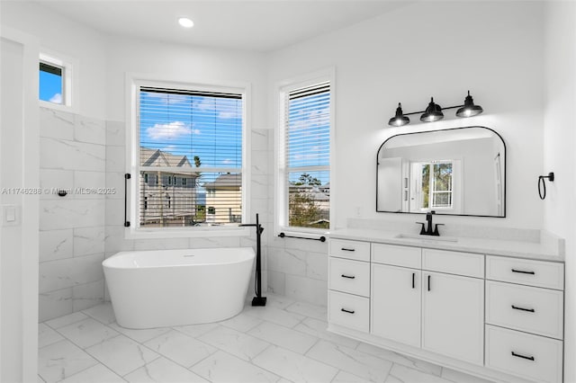 bathroom with a wealth of natural light, marble finish floor, a soaking tub, and vanity