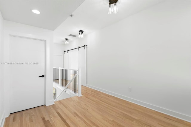 spare room with a barn door, wood finished floors, visible vents, and baseboards