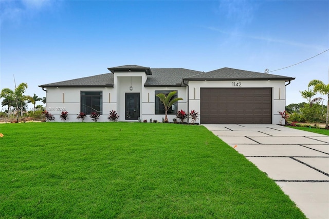 prairie-style home with an attached garage, a shingled roof, concrete driveway, stucco siding, and a front lawn