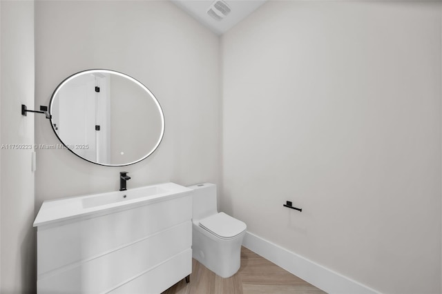 bathroom with toilet, wood finished floors, visible vents, vanity, and baseboards