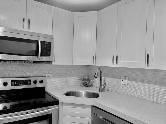 kitchen featuring stainless steel appliances, light countertops, decorative backsplash, white cabinetry, and a sink