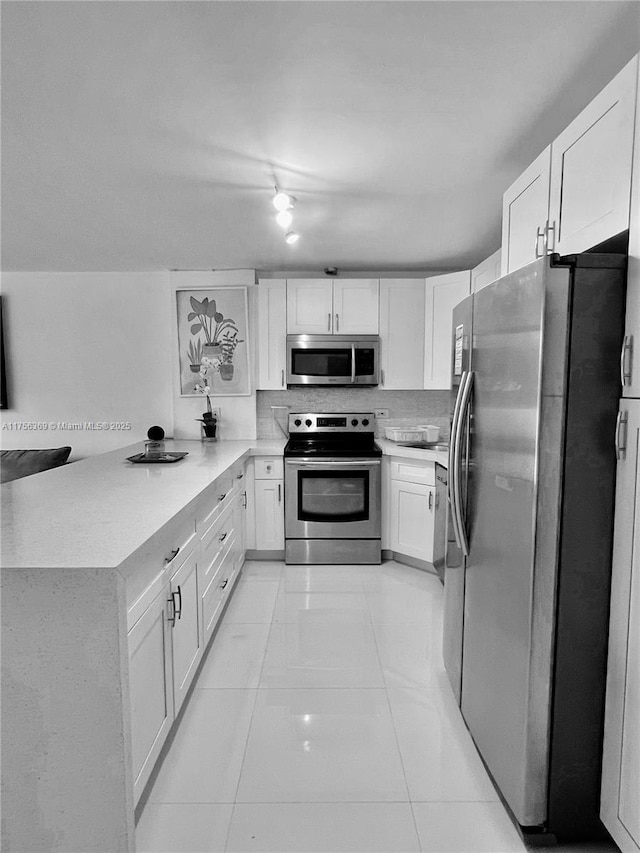 kitchen featuring white cabinets, a peninsula, stainless steel appliances, backsplash, and light tile patterned flooring