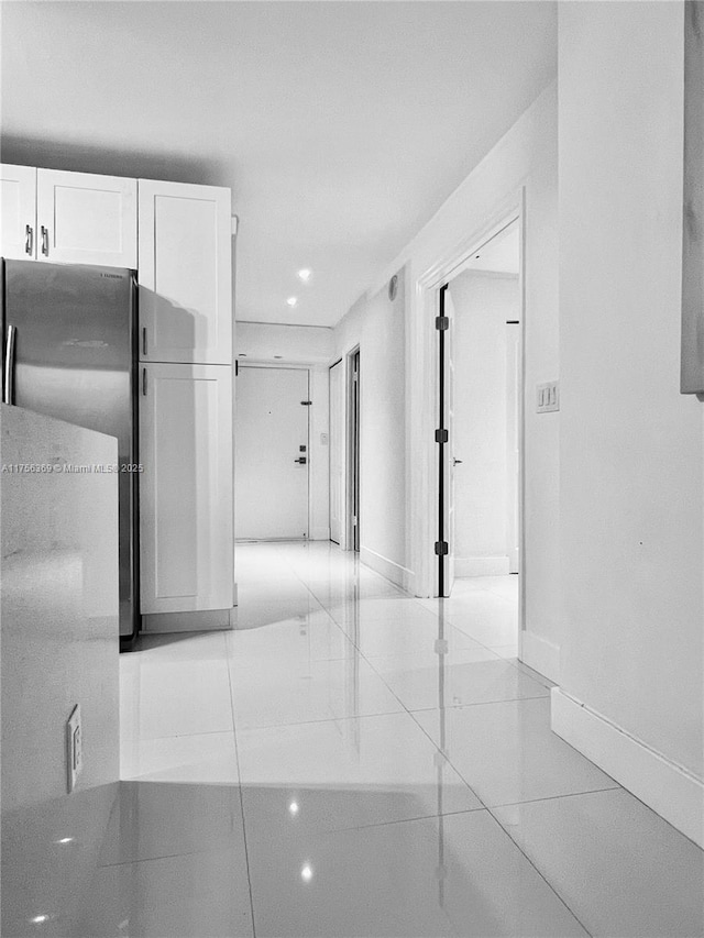 kitchen with light tile patterned floors, freestanding refrigerator, white cabinetry, and baseboards