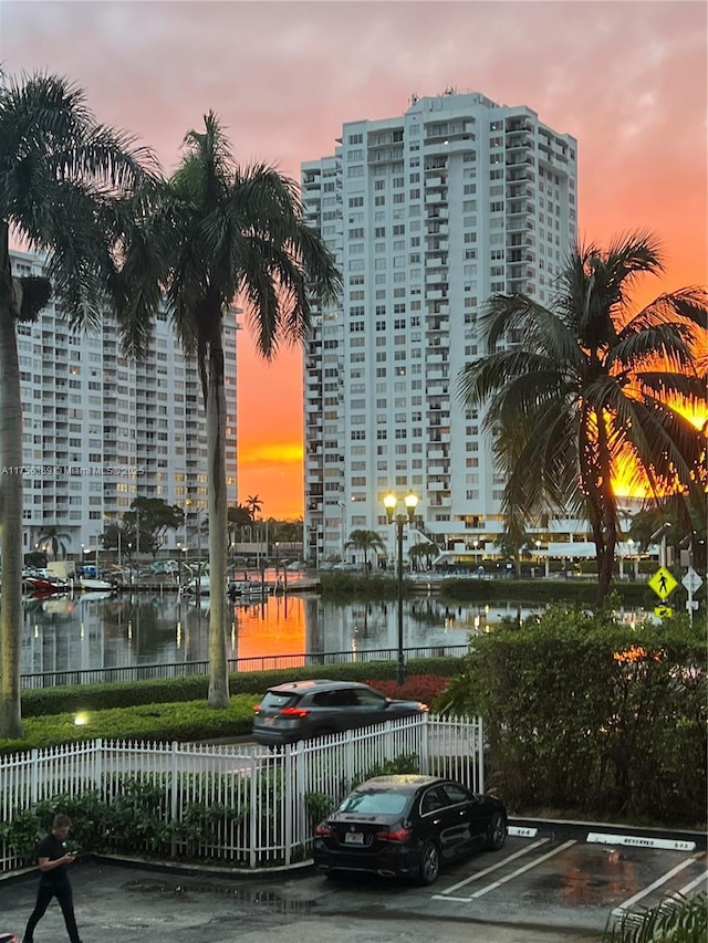 property at dusk featuring a water view, uncovered parking, and fence