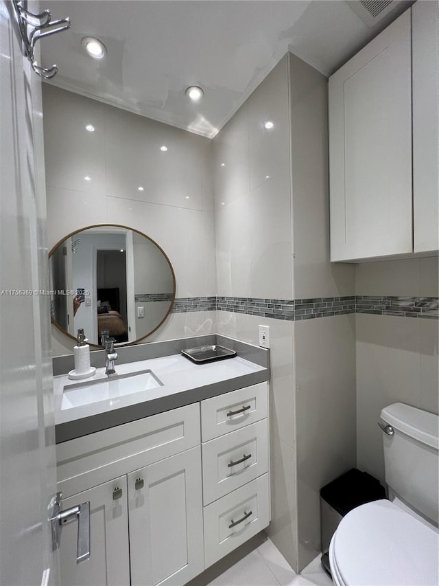 bathroom with tile walls, recessed lighting, toilet, connected bathroom, and vanity