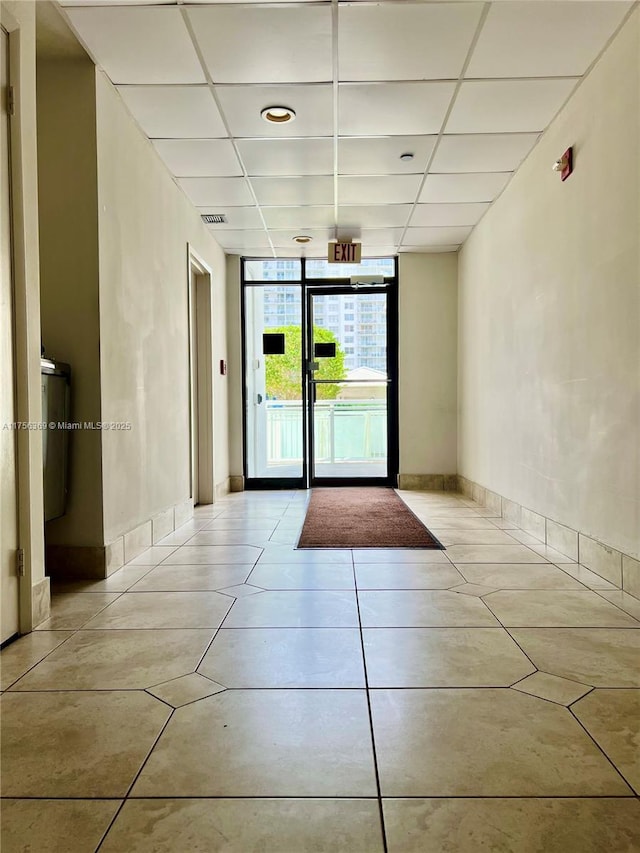 interior space with expansive windows, light tile patterned floors, a paneled ceiling, and baseboards