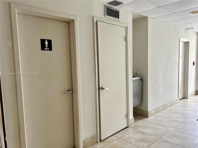 corridor with a paneled ceiling, visible vents, baseboards, and light tile patterned flooring