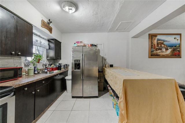 kitchen with light tile patterned floors, stainless steel appliances, a sink, a textured ceiling, and dark cabinets