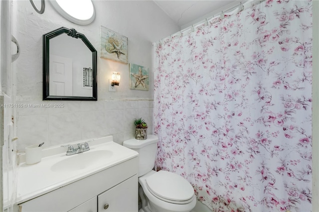 bathroom with toilet, a shower with shower curtain, vanity, and tile walls