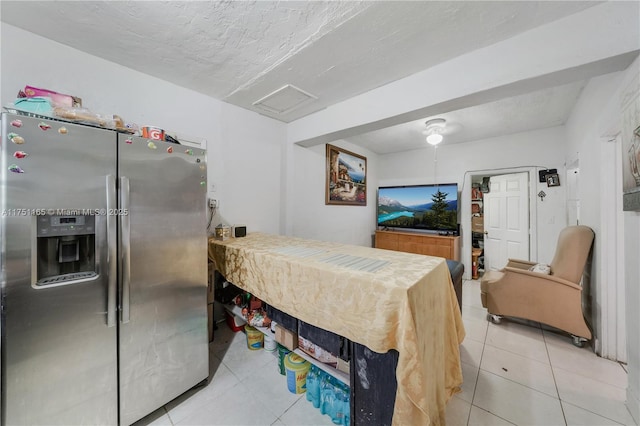 bedroom with light tile patterned floors, attic access, a textured ceiling, and stainless steel fridge with ice dispenser