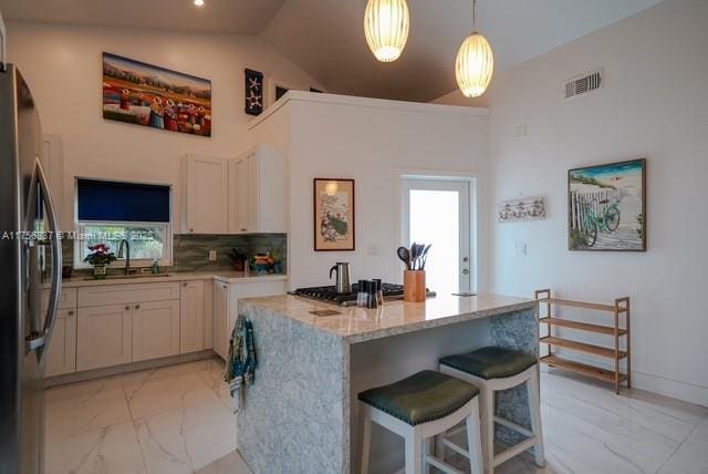 kitchen with a sink, freestanding refrigerator, visible vents, marble finish floor, and light stone countertops