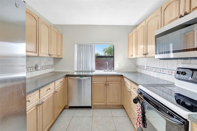 kitchen with light tile patterned flooring, light brown cabinets, a sink, appliances with stainless steel finishes, and backsplash