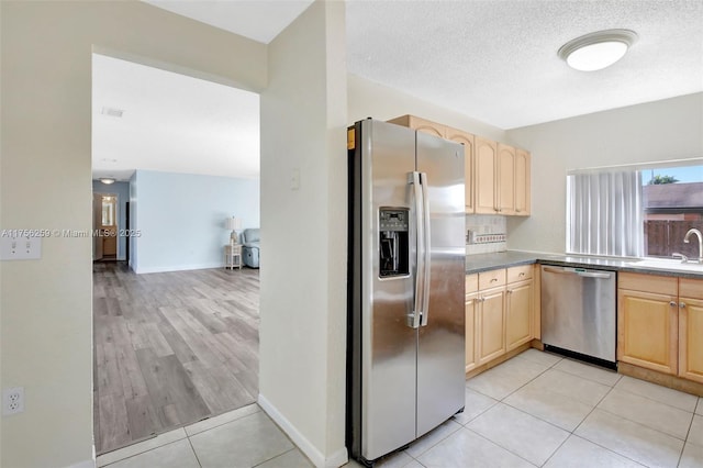 kitchen with a sink, stainless steel appliances, a textured ceiling, and light brown cabinets