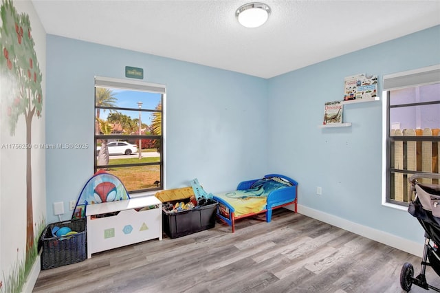 rec room featuring a textured ceiling, baseboards, and wood finished floors