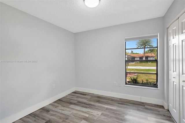 empty room with a textured ceiling, baseboards, and wood finished floors