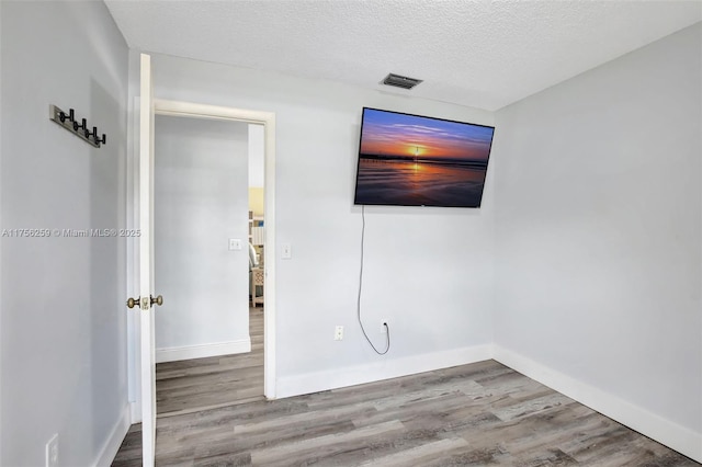 empty room featuring a textured ceiling, wood finished floors, visible vents, and baseboards