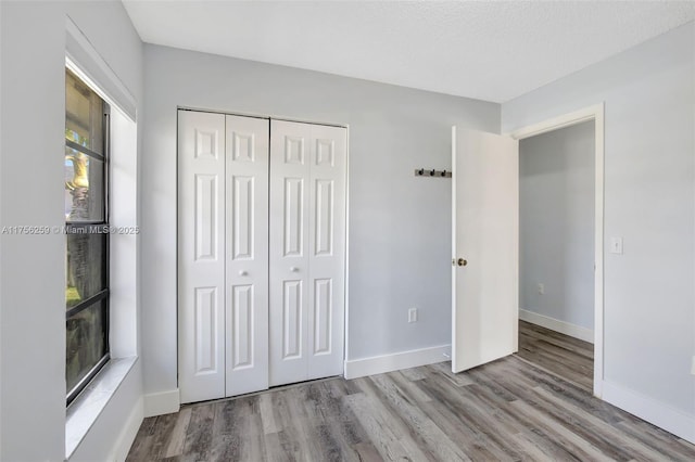 unfurnished bedroom with a textured ceiling, a closet, wood finished floors, and baseboards